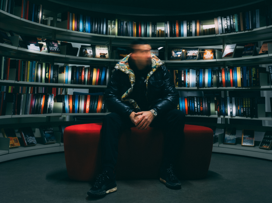 Abdullah Hassan sidder på en rød puf med bogreoler i baggrunden. Billedet er sløret, så man ikke kan se hans ansigt tydeligt.  